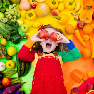 Menina no meio de muitas frutas e legumes, indicando reeducação Alimentar