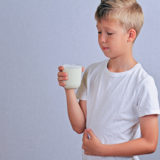 menino com copo de leite na mão e dor abdominal indicando intolerancia alimentar na infancia